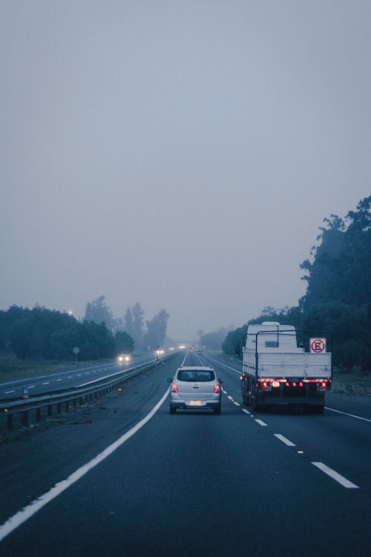 A misty stretch of highway at dawn with faint traffic ahead