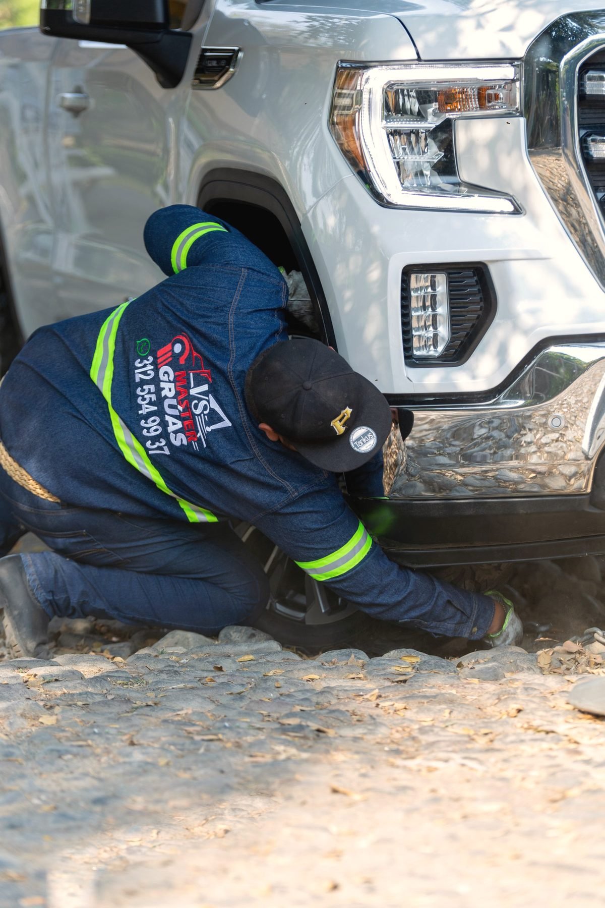 An operator crouched at the front wheel of a pickup during a recovery
