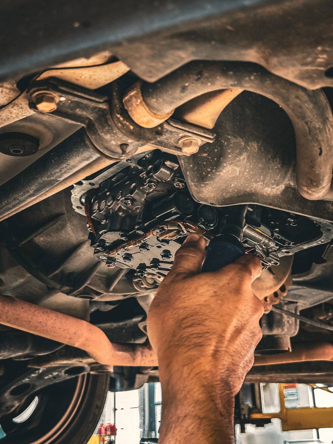 A hand reaching up to inspect the underside of a raised vehicle