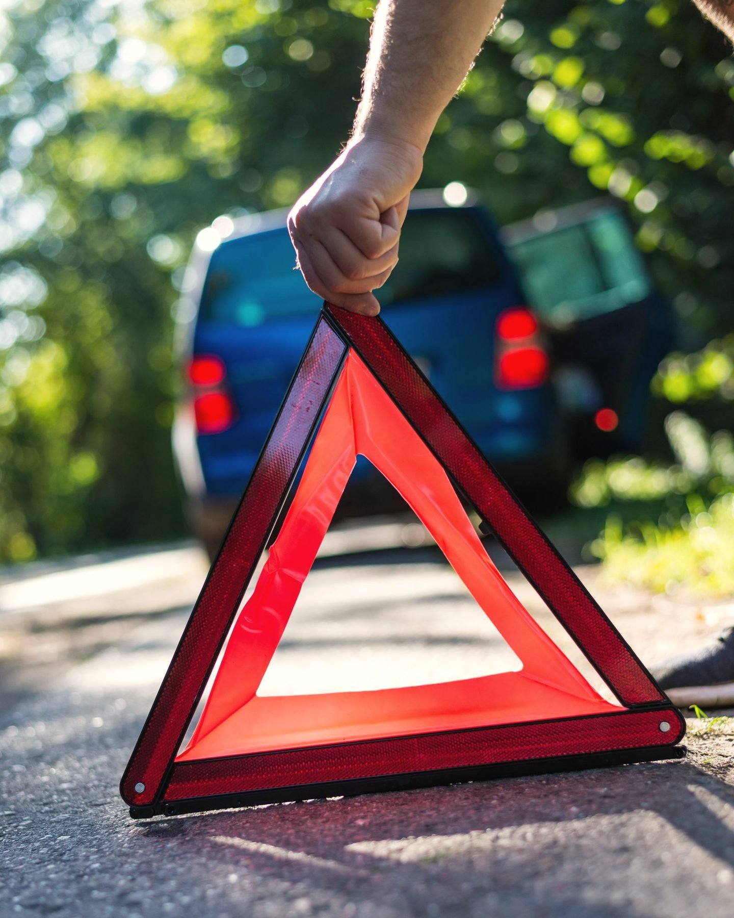 A red reflective warning triangle set on the road behind a stopped car